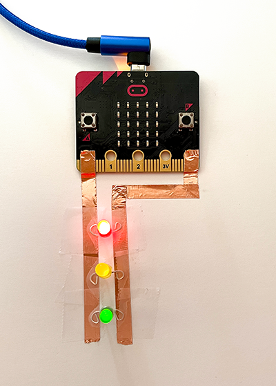 two pieces of copper tape attached to the micro:bit with illuminated LEDs
